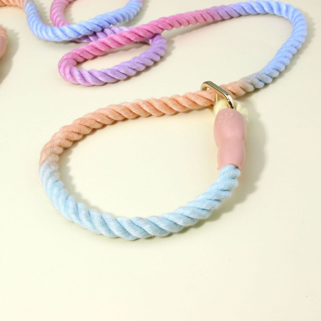 Rope slip lead close-up of the twisted rope, gold-coloured ring and pink rubber stopper on a cream surface