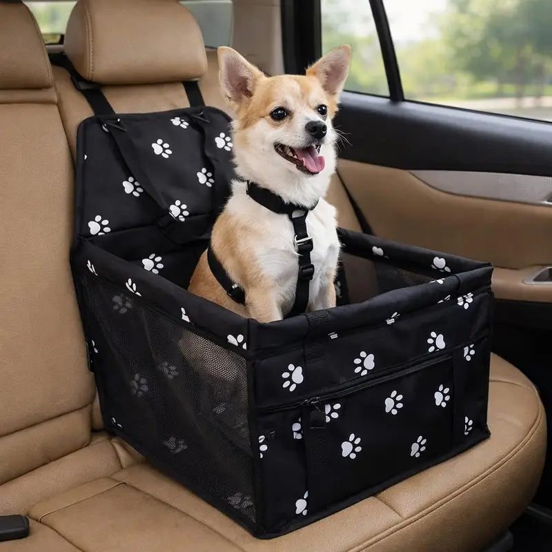 Black paw-print dog car booster seat on a car seat, with a small tan dog sitting in it clipped to the lead