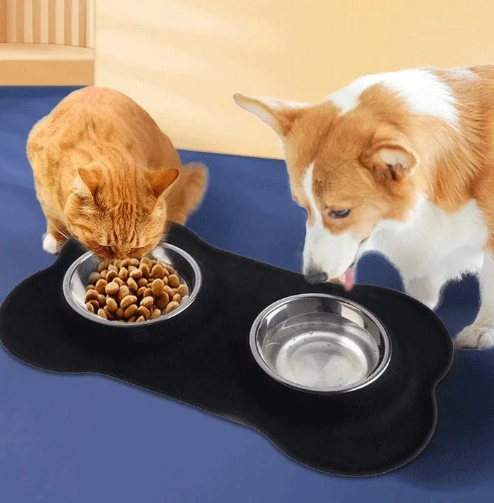 Black bone-shaped silicone mat with two steel bowls and a dog eating from them