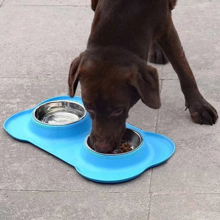 Blue bone-shaped silicone mat with two steel bowls, a chocolate Labrador eating from it